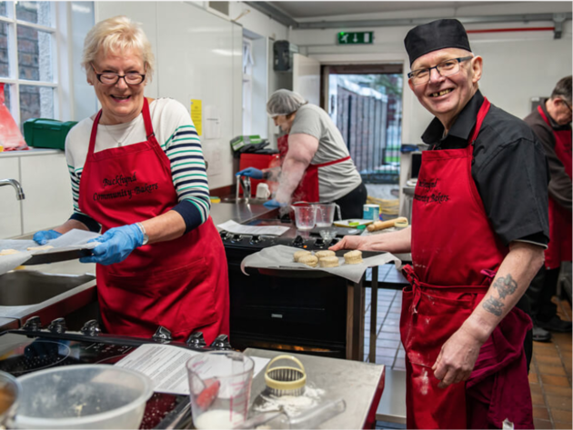 Two participants in chef equipment cooking in a kitchen 